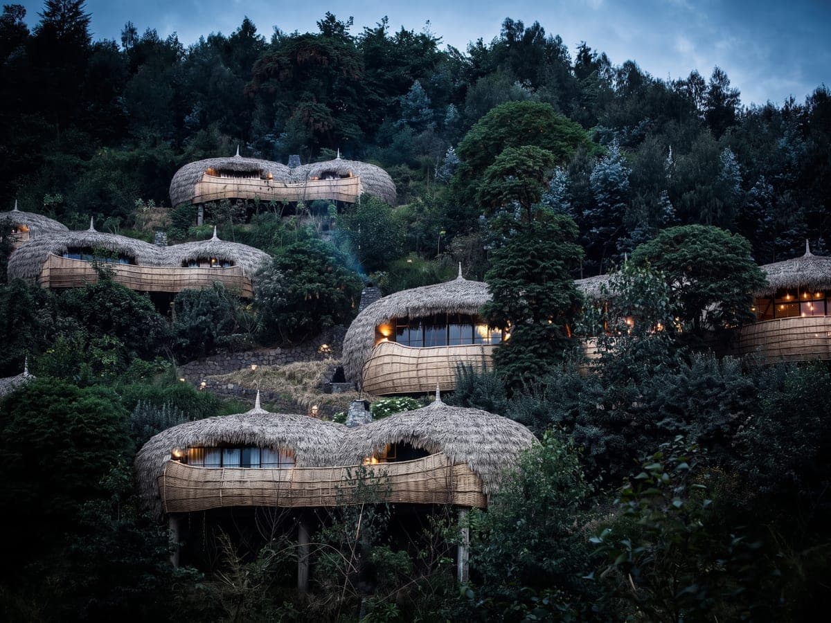 فلل مستديرة بأسقف من القش وشرفات من الخيزران المجدول على سفح تلّ مكسوّ بالغابات عند الغسق، والأضواء الدافئة في نوافذها